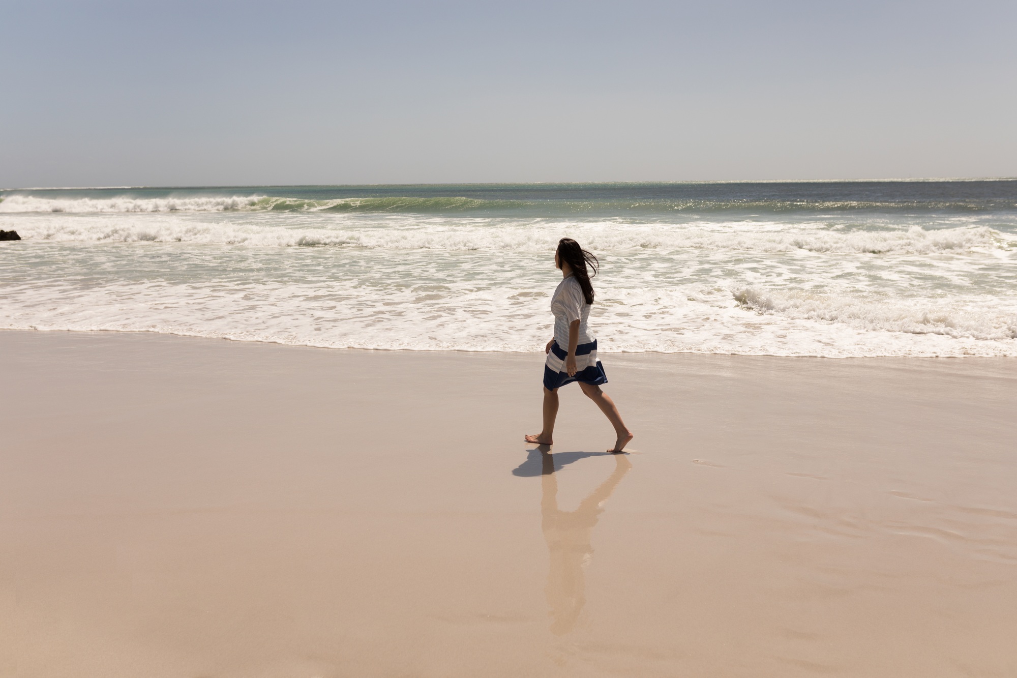 Side view of young woman walking on beach and looking at the horizon in the sunshine